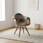 Eames-style patchwork armchair featuring a molded shell seat upholstered in vibrant multi-patterned fabric patchwork with integrated curved armrests, supported by dark wood legs and black metal Eiffel wire bracing.
