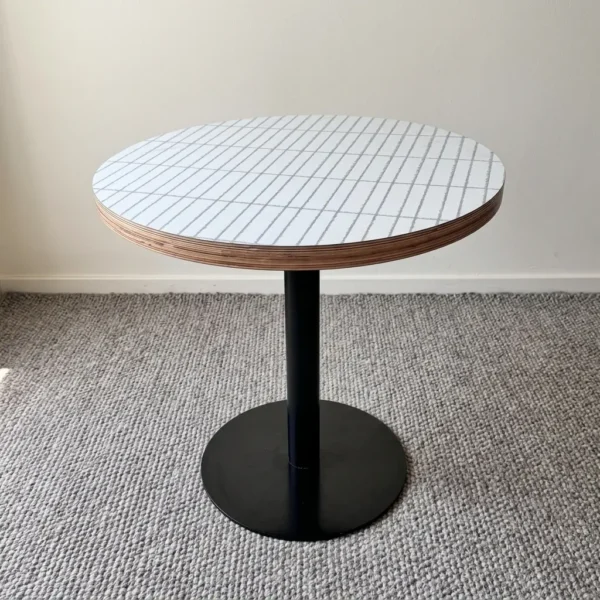 Round dining table featuring a white top with a subtle linear pattern and exposed layered plywood edge detail, supported by a central black metal pedestal pole and a sturdy flat circular base.