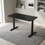 Height adjustable electric table featuring a sleek matte black desktop with dual cable management grommets, an under-desk digital control keypad, and heavy-duty black motorized telescoping legs supported by T-style flat feet.