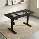 Height adjustable electric table featuring a sleek matte black desktop with dual cable management grommets, an under-desk digital control keypad, and heavy-duty black motorized telescoping legs supported by T-style flat feet.