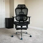 Orthopedic office chair with footrest featuring full black mesh upholstery, an adjustable curved headrest, split dual-backrest ergonomic lumbar support, 3D adjustable armrests, a fold-away padded leg rest, and a polished chrome five-star base with blue accent swivel casters.
