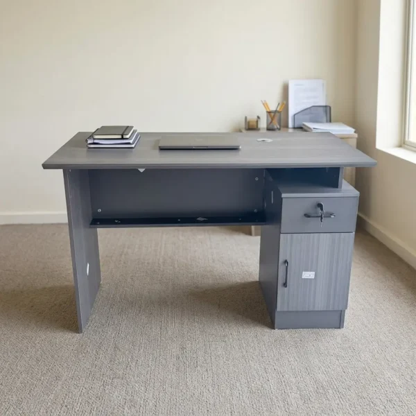 Executive 1200mm office desk featuring a dark grey wood-grain laminate finish, a rectangular tabletop with an integrated cable grommet, a full modesty panel, and an integrated right-side pedestal unit with an open top compartment, a lockable drawer with key, and a lower storage cabinet.