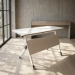 120cm foldable training table featuring a rectangular white laminate tabletop with a black edge band, integrated onto a white metal nesting frame with a matching solid white modesty panel, supported by angled T-legs equipped with dual-wheel locking casters.