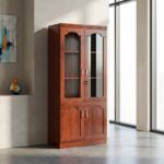 2-door office file cabinet featuring a tall wooden structure with a rich reddish-brown cherry wood grain finish, designed with an upper display section with arched glass-paneled doors enclosing interior storage shelves, and a lower base cupboard with twin solid wood doors, all accented by slim vertical silver handles.