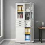 White office cabinet with safe featuring a clean white finish, top display section with two glass-framed lockable doors, middle section equipped with three small pull-out drawers alongside a lockable safe compartment, and a bottom storage section with two solid doors with vertical handles and key locks.