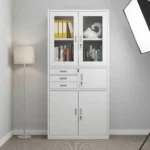 White office cabinet with safe featuring a clean white finish, top display section with two glass-framed lockable doors, middle section equipped with three small pull-out drawers alongside a lockable safe compartment, and a bottom storage section with two solid doors with vertical handles and key locks.