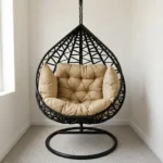 High quality hammock swing featuring a teardrop-shaped dark brown woven wicker egg chair, a thick tufted beige cushion set, and a heavy-duty black metal hanging stand with a circular base.