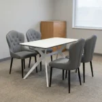 4-seater dining set featuring a rectangular white marble-patterned tabletop with white geometric angled metal legs, paired with four grey leatherette upholstered chairs with button-tufted inner backrests and tapered black legs.