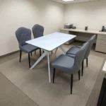 4-seater dining set featuring a rectangular white marble-patterned tabletop with white geometric angled metal legs, paired with four grey leatherette upholstered chairs with button-tufted inner backrests and tapered black legs.