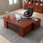 Executive 2m office table featuring a rich mahogany wood grain finish, an inset black leatherette writing pad with integrated wire management grommets, a patterned front modesty panel with leatherette accent panels, sturdy pedestal end legs on dark bases, and an attached side return cabinet.