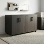 4-door wooden office cupboard featuring a dark charcoal grey wood grain finish, four hinged swing doors with sleek black vertical handles, a low-profile credenza silhouette, internal divided shelving units, and a mobile base equipped with heavy-duty caster wheels.