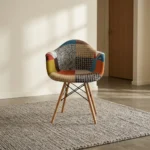 Fabric multicolor eames chair featuring vibrant patchwork fabric upholstery with geometric and houndstooth patterns, a contoured armchair shell with integrated armrests, natural wooden legs, and black Eiffel-style metal wire cross-bracing.