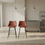 Leather kitchen bar stool featuring warm cognac brown faux leather upholstery with vertical channel tufting, a low-profile ergonomic backrest, and slim matte black metal legs with integrated footrest rungs.