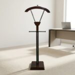 Modern wooden office coat hanger featuring a rich mahogany-finished wood construction, a contoured upper jacket hanger supported by metallic V-struts, a horizontal trouser bar, and a sturdy square base.
