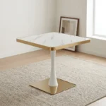 Modern square dining table featuring a white faux marble top with polished gold metallic edging, supported by a central white tulip pedestal column and a heavy flat square brass-toned base.