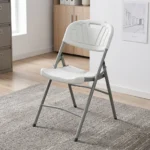 Heavy duty white foldable chair featuring a blow-molded high-density white plastic seat and backrest with a decorative fan motif and built-in carrying handle, supported by a sturdy powder-coated grey steel folding frame with cross-bracing and non-marring foot caps.