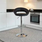Leather swivel barstool featuring a rounded cutout backrest upholstered in smooth black faux leather, an adjustable gas-lift hydraulic pedestal base in polished chrome, an integrated semi-circular footrest, and a sturdy round trumpet base.