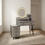 Modern dressing table with LED featuring a circular touch-sensor illuminated vanity mirror, a grey faux-marble tabletop, fluted grey drawer fronts with black handles, built-in display shelves, dark tapered legs with gold accents, and a side three-drawer storage chest.