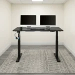 Electric height adjustable table featuring a spacious matte black rectangular desktop, digital push-button LED keypad controller, integrated side accessory headphone hook, motorized dual telescoping steel lifting columns, and a heavy-duty black steel T-frame base.