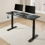 Electric height adjustable table featuring a spacious matte black rectangular desktop, digital push-button LED keypad controller, integrated side accessory headphone hook, motorized dual telescoping steel lifting columns, and a heavy-duty black steel T-frame base.