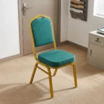 Stackable green conference chair featuring diamond-patterned emerald green upholstered fabric with subtle white dot accents, a cushioned crown-back seat and backrest, top integrated handle grip, and a sturdy metallic gold-painted steel frame with protective floor glides.