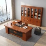 160cm executive office table featuring a rich mahogany wood finish, integrated black leatherette writing inlay, built-in cable management ports, decorative front modesty panel with geometric dark charcoal inlay and center diamond motif, and an L-shaped side return credenza with lockable storage drawers and open shelving.