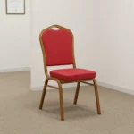 Stackable red conference chair featuring diamond-patterned bright red upholstered fabric with subtle white dot accents, a cushioned crown-back seat and backrest, top integrated handle grip, and a sturdy metallic gold-painted steel frame with non-marring floor glides.