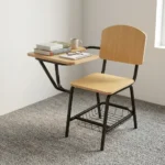 Wooden student study chair featuring light natural oak plywood seat and backrest panels, an attached right-hand tablet writing desk with rounded corners, a tubular black metal frame, and an under-seat wire mesh book basket.