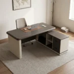 Spacious 1.6m office table featuring a two-tone grey wood-grain and cream laminate surface with rounded edges, a rectangular cable management outlet, an L-shaped side return credenza with open shelving and lockable drawers, and a decorative front modesty panel with a distinctive wave-pattern accent.