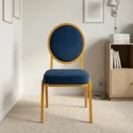 Armless blue conference chair featuring navy blue fabric upholstery with white dot pattern, a oval medallion backrest, a cushioned seat, and a stackable gold-finished metal frame with straight legs and floor glides.