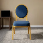 Armless blue conference chair featuring navy blue fabric upholstery with white dot pattern, a oval medallion backrest, a cushioned seat, and a stackable gold-finished metal frame with straight legs and floor glides.