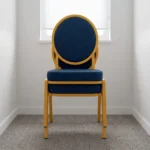 Armless blue conference chair featuring navy blue fabric upholstery with white dot pattern, a oval medallion backrest, a cushioned seat, and a stackable gold-finished metal frame with straight legs and floor glides.