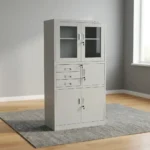 Steel cabinet with safe featuring a powder-coated light grey finish, a top double-door glass display cabinet with key lock, a middle section with three drawers alongside a locked safe compartment, and a bottom double steel-door storage locker with key lock.