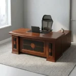 Mahogany 1.6m executive desk featuring a rich wood veneer finish with bevelled edge detailing, an inset black leatherette writing pad, dual desktop cable management grommets, an ornate decorative front modesty panel with black leatherette inlay and circular wood accents, and thick pedestal leg supports.