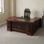Mahogany 1.6m executive desk featuring a rich wood veneer finish with bevelled edge detailing, an inset black leatherette writing pad, dual desktop cable management grommets, an ornate decorative front modesty panel with black leatherette inlay and circular wood accents, and thick pedestal leg supports.