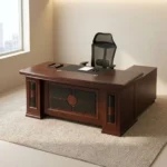Mahogany 1.6m executive desk featuring a rich wood veneer finish with bevelled edge detailing, an inset black leatherette writing pad, dual desktop cable management grommets, an ornate decorative front modesty panel with black leatherette inlay and circular wood accents, and thick pedestal leg supports.