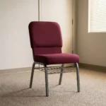 Fabric stackable church chair featuring plush burgundy fabric upholstery with a padded rectangular backrest and waterfall seat design, an armless ergonomic profile, an under-seat metal wire book rack, and a durable silver powder-coated steel frame with protective floor glides.