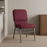Fabric stackable church chair featuring plush burgundy fabric upholstery with a padded rectangular backrest and waterfall seat design, an armless ergonomic profile, an under-seat metal wire book rack, and a durable silver powder-coated steel frame with protective floor glides.