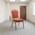 Fabric stackable conference chair featuring patterned red and gold patterned fabric upholstery, high-density padded seat and crown-back cushion, an armless space-saving stackable frame, an integrated top hand-hold, and a gold powder-coated square steel tube frame with bumper guards and floor glides.