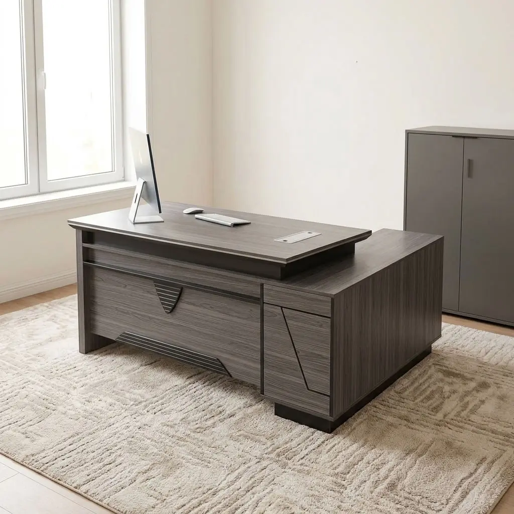 Executive 2.0m L-shaped office desk featuring a dark grey wood-grain laminate finish, dual flip-top desktop cable management grommets, a stylized front modesty panel with black geometric accent detailing, a integrated side return extension unit with drawer storage, and solid panel-style engineered wood base supports.