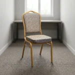 Comfortable armless fabric conference chair featuring patterned beige fabric upholstery over a thick padded seat cushion and backrest, an armless stackable crown-back frame design with an integrated top hand-hold handle, and a durable gold powder-coated square steel four-legged base.