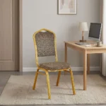 Fabric conference event chair featuring patterned beige fabric upholstery over a thick padded seat cushion and backrest, an armless stackable crown-back frame design with an integrated top hand-hold handle, and a durable gold powder-coated square steel four-legged base.