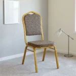 Fabric conference event chair featuring patterned beige fabric upholstery over a thick padded seat cushion and backrest, an armless stackable crown-back frame design with an integrated top hand-hold handle, and a durable gold powder-coated square steel four-legged base.
