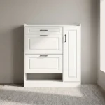 White modern shoe rack featuring crisp white engineered wood with traditional recessed panel detailing, a top utility pull-out drawer, two tilt-down shoe compartment drawers, a tall side cabinet door with slim black handles, an open lower shoe storage shelf, and a flat plinth base.