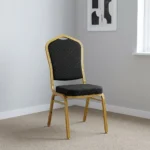 Black stackable event chair featuring black patterned fabric upholstery with gold dot accents on a crown-back backrest and padded seat cushion, an armless space-saving frame, and a durable gold powder-coated aluminum steel tubular frame base with stack bumpers and floor glides.