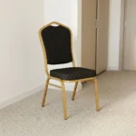 Black stackable event chair featuring black patterned fabric upholstery with gold dot accents on a crown-back backrest and padded seat cushion, an armless space-saving frame, and a durable gold powder-coated aluminum steel tubular frame base with stack bumpers and floor glides.