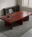 3M mahogany boardroom table featuring a large 3000mm rectangular rich reddish-brown mahogany wood laminate tabletop with diagonal corner seam detailing, a central black wire management trough with pop-up power/data modules, and a sturdy triple panel-leg base with integrated modesty cross-bracing.