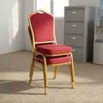High quality red banquet chair featuring a crown-back profile with red fabric upholstered backrest and a high-density cushioned seat pan, a stackable armless frame design with protective stacking bumpers, and a gold powder-coated square steel tube four-leg base with non-marring floor glides.