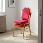 High quality red banquet chair featuring a crown-back profile with red fabric upholstered backrest and a high-density cushioned seat pan, a stackable armless frame design with protective stacking bumpers, and a gold powder-coated square steel tube four-leg base with non-marring floor glides.
