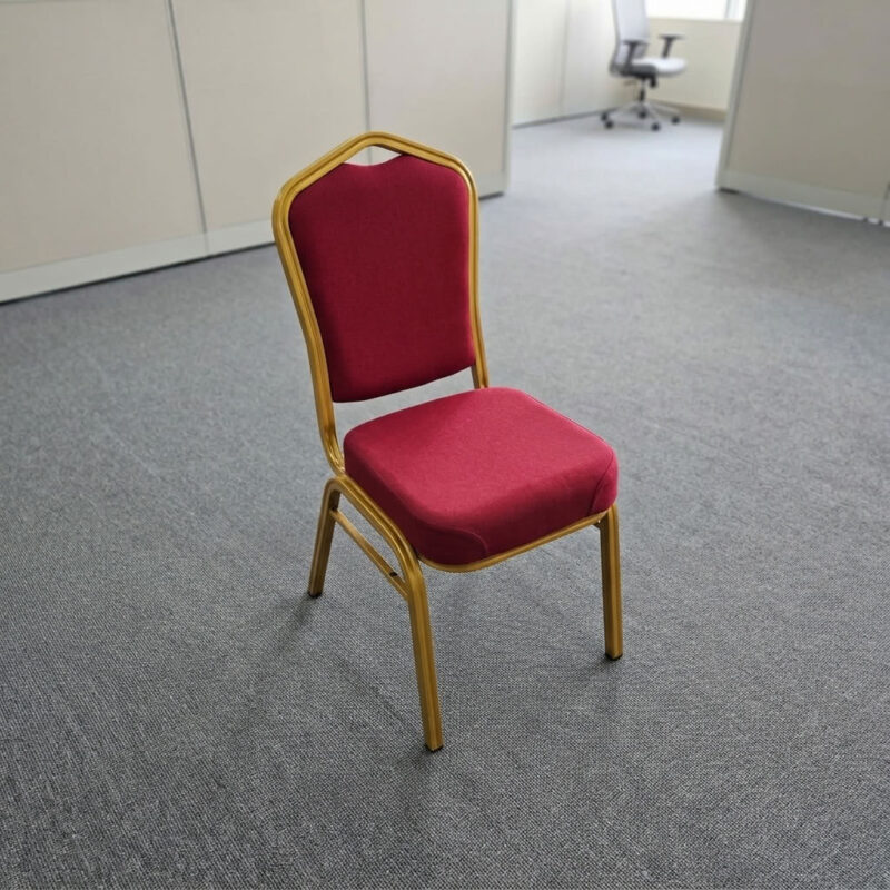 Red fabric stackable event chair featuring rich crimson red fabric upholstery, a high-density padded crown-back backrest with integrated top handhold cut-out and thick cushioned seat, armless space-saving stackable design with frame bumper guards, and a heavy-duty metallic gold powder-coated tubular steel four-legged frame equipped with protective floor glides. Red fabric stackable event chair featuring rich crimson red fabric upholstery, a high-density padded crown-back backrest with integrated top handhold cut-out and thick cushioned seat, armless space-saving stackable design with frame bumper guards, and a heavy-duty metallic gold powder-coated tubular steel four-legged frame equipped with protective floor glides.